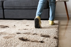 Little girl in muddy shoes messing up carpet at home