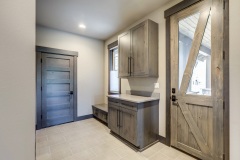 Back room with storage cabinets and sitting bench between outside and garage and grey tiles.